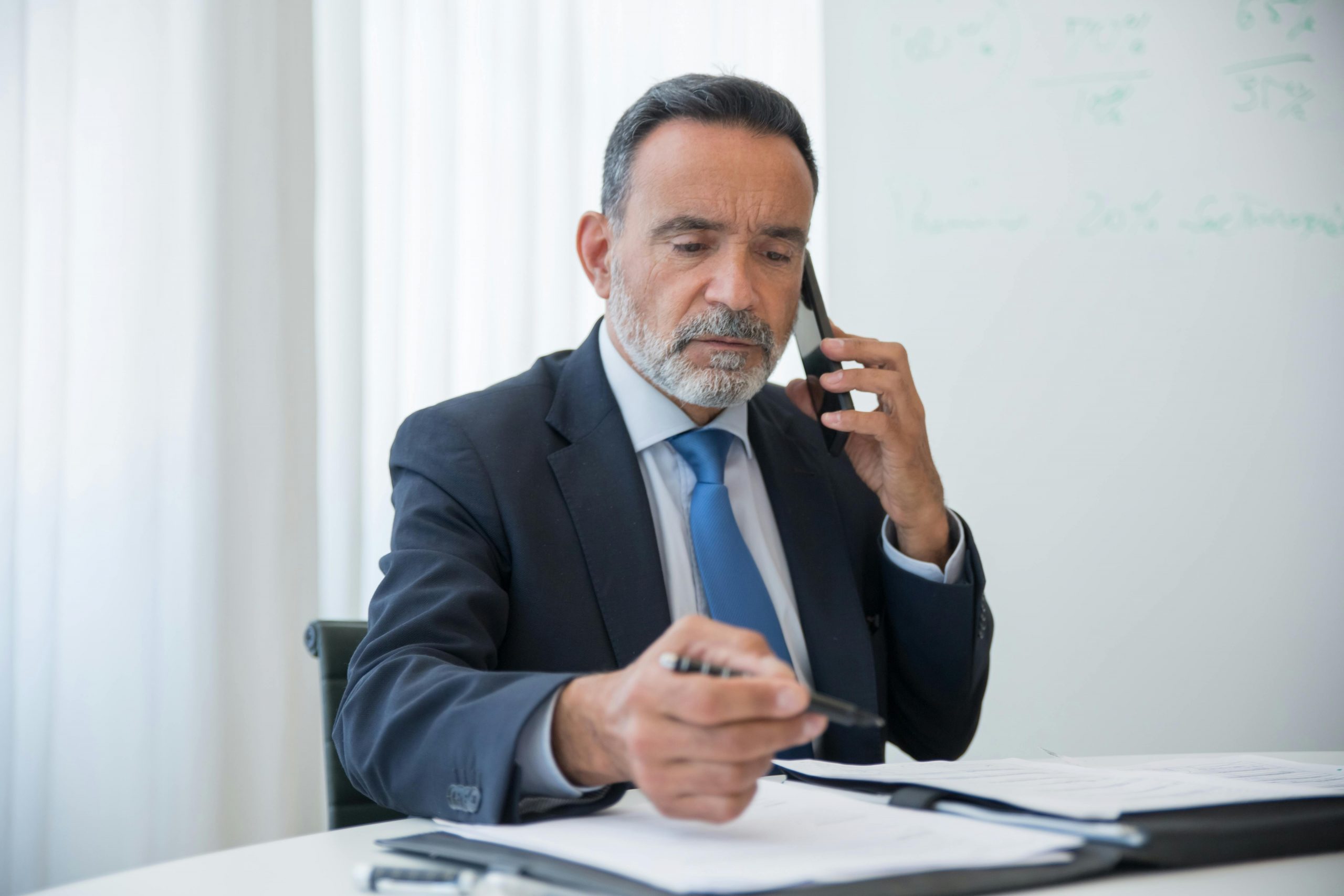 elderly businessman writing while speaking on the phone