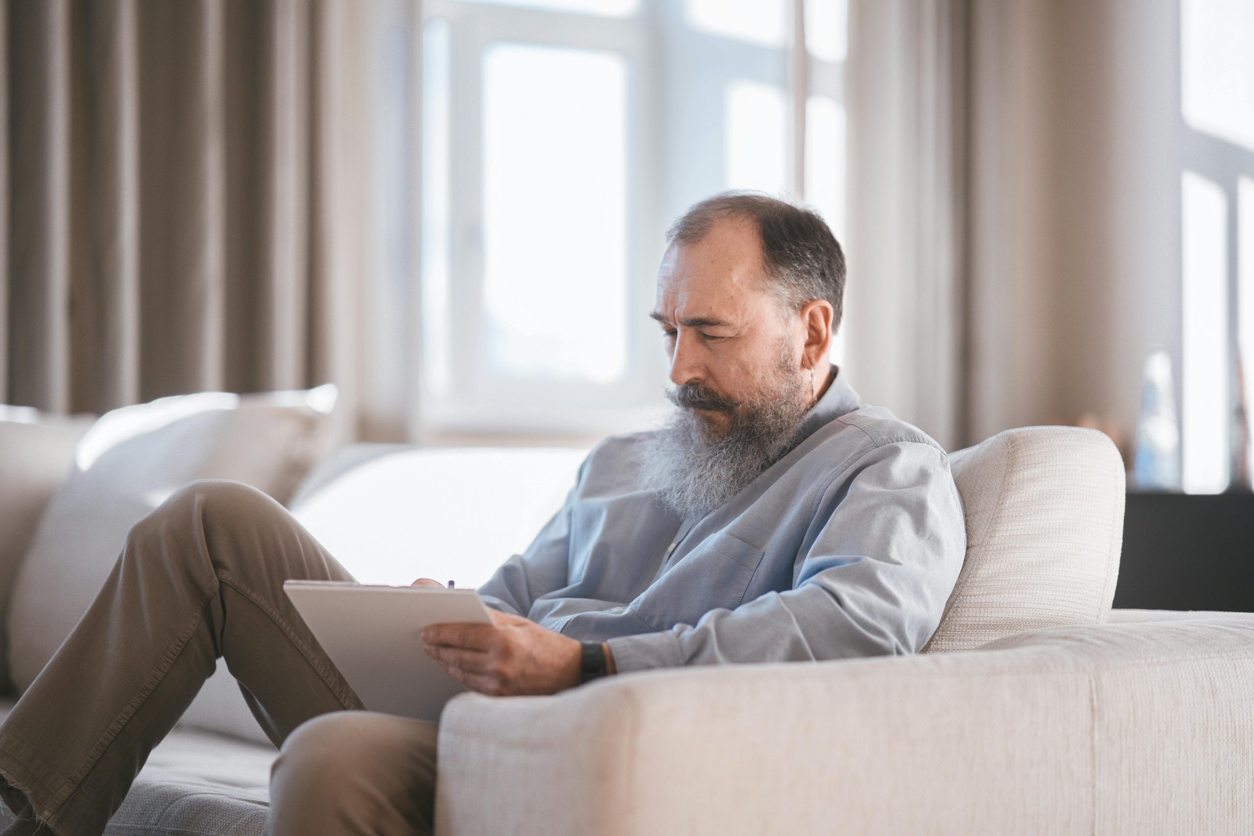 elderly man writing while seated on a couch