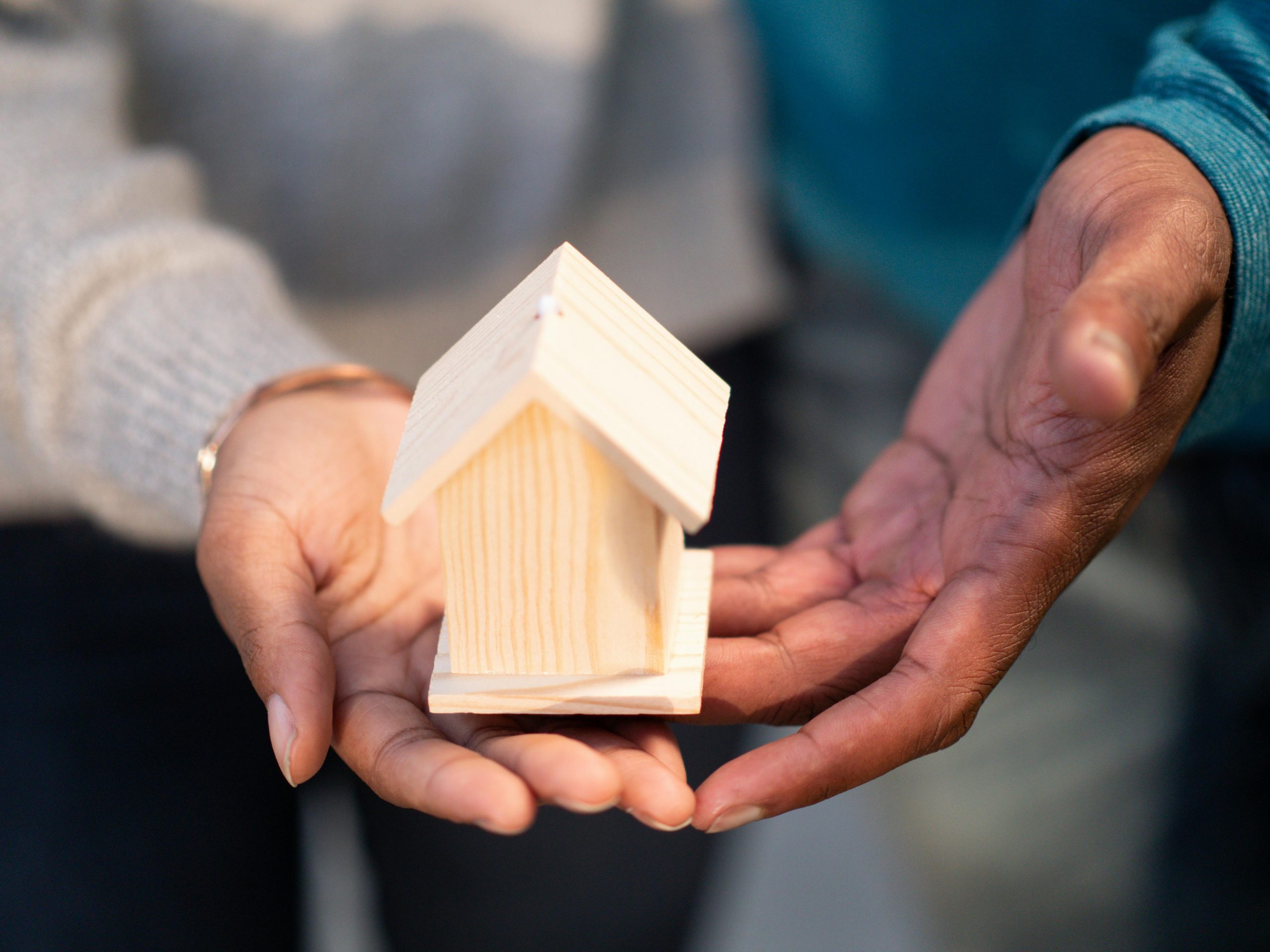 wooden miniature house resting on a couple's hands